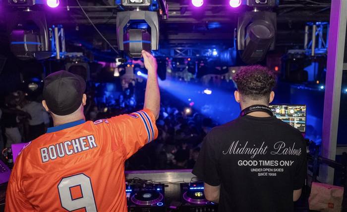 Two DJs performing at a nightclub with a packed crowd