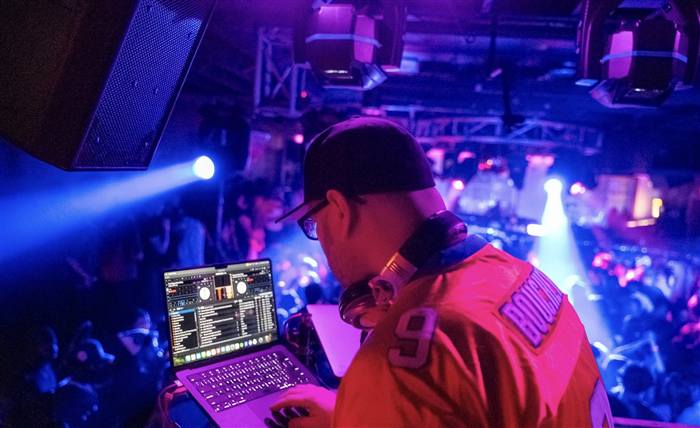 Close-up of a DJ mixing at a nightclub overlooking the crowd