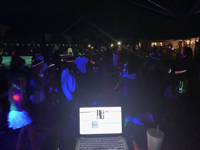 Nighttime glow-stick dance party with DJ booth in foreground