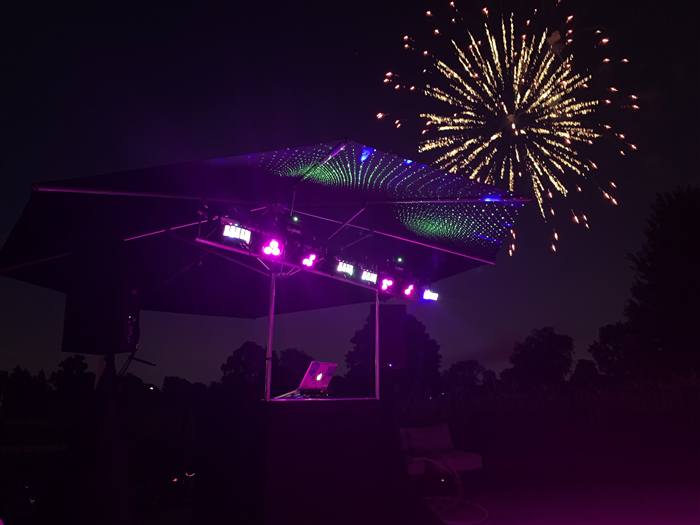 DJ light rig silhouetted against fireworks at an outdoor event